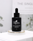 Black serum bottle labeled 'R Labs Cosmetics Glutathione Serum' on a white surface with a blurred background.